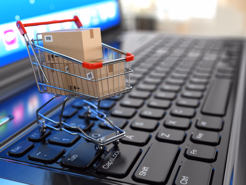Carrinho de compras em miniatura com caixas de papelão sobre o teclado de um notebook