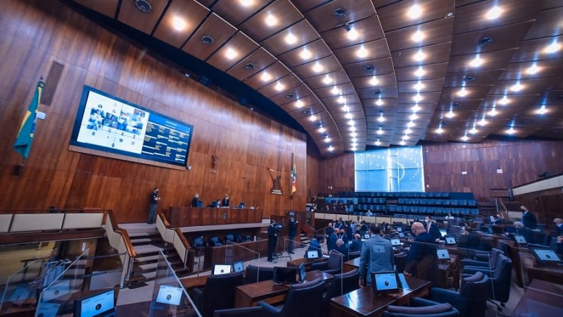 Plenário de assembleia legislativa com teto de madeira, luzes e telão ao fundo