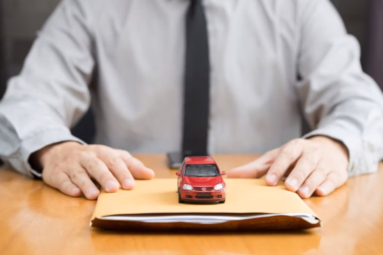 Homem de camisa e gravata com um carrinho vermelho em miniatura sobre um envelope na mesa