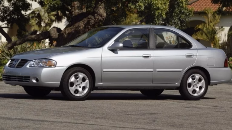 Nissan Sentra prata estacionado em rua arborizada, visto de lado