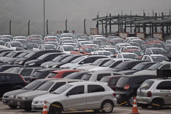 Pátio lotado de carros estacionados em fileiras, com estrutura metálica ao fundo