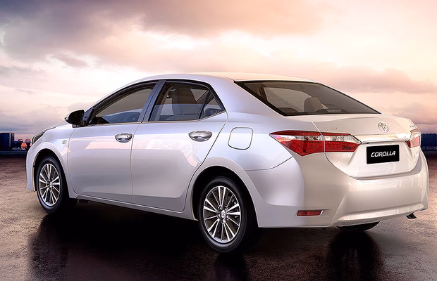 Toyota Corolla prata visto de traseira lateral, com céu de entardecer ao fundo