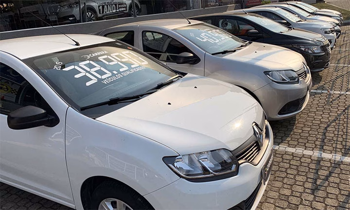 Renault Sandero branco com preço escrito no para-brisa, estacionado em pátio de loja