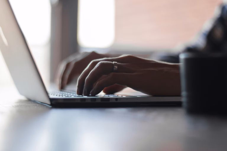 Mãos digitando no teclado de um notebook sobre mesa clara
