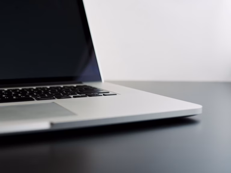 Notebook prata aberto sobre mesa escura, com parede branca ao fundo