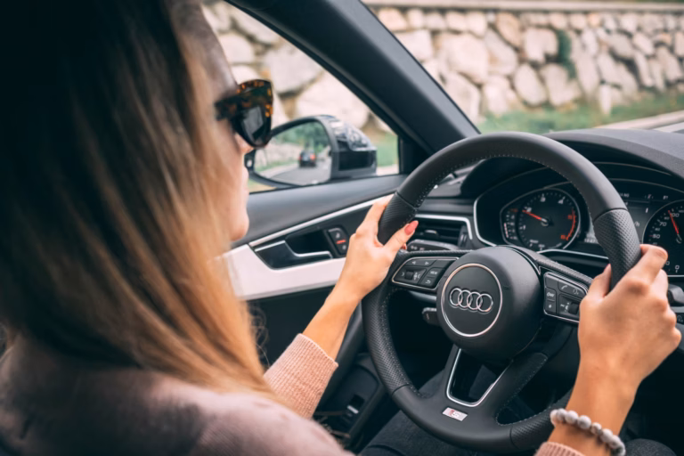 Mulher de óculos escuros dirigindo um carro da Audi com as duas mãos no volante