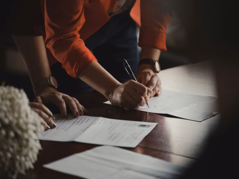 Duas pessoas assinando documentos em papel sobre uma mesa escura