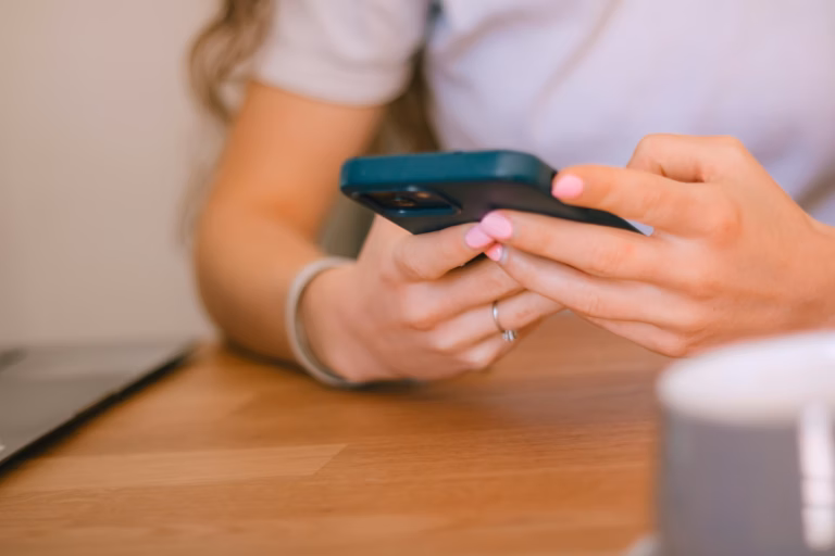Mãos de mulher segurando um celular sobre uma mesa de madeira