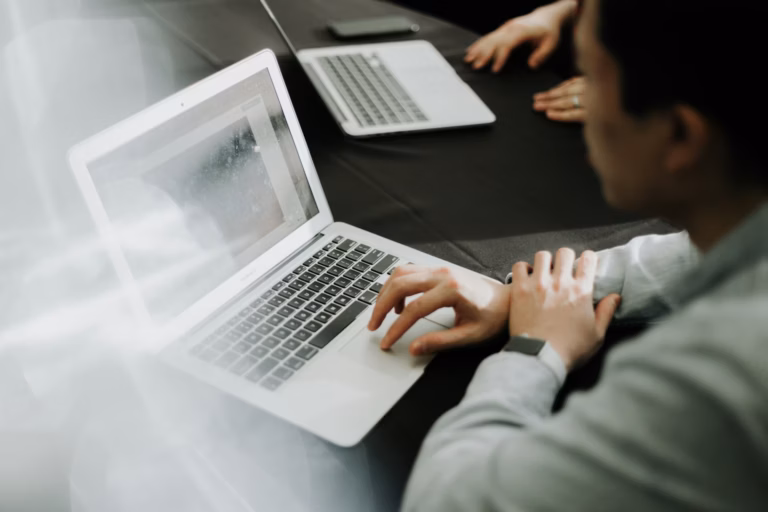 Duas pessoas trabalhando em notebooks sobre uma mesa escura, vistas de cima