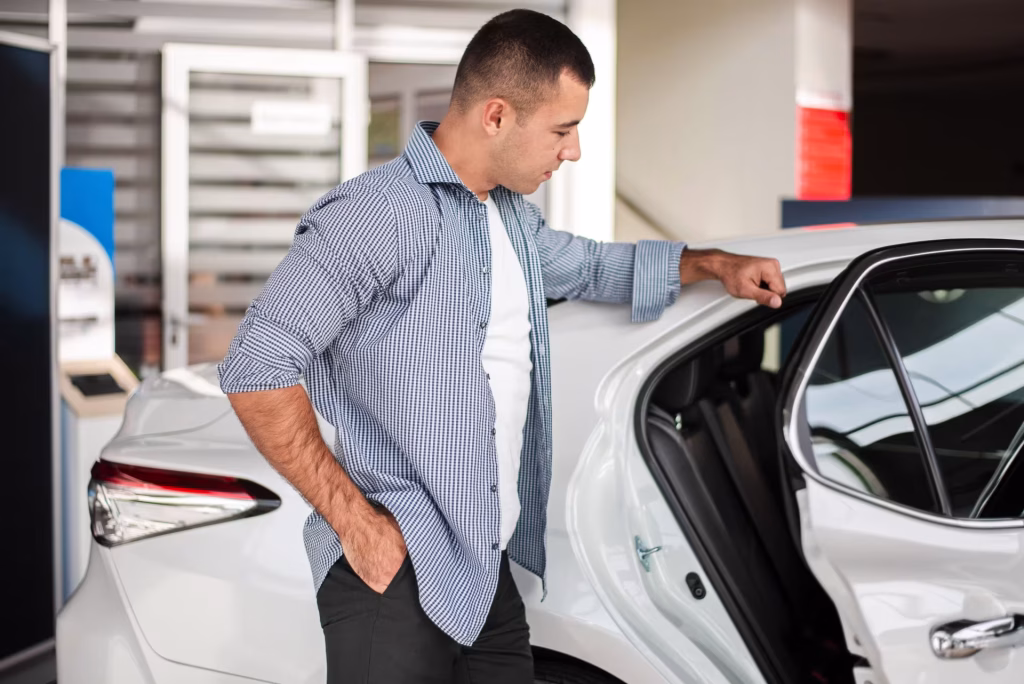 Homem conferindo um carro branco com a porta aberta no showroom