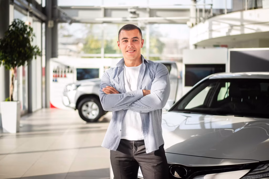 Homem sorridente de braços cruzados no meio de um showroom de carros