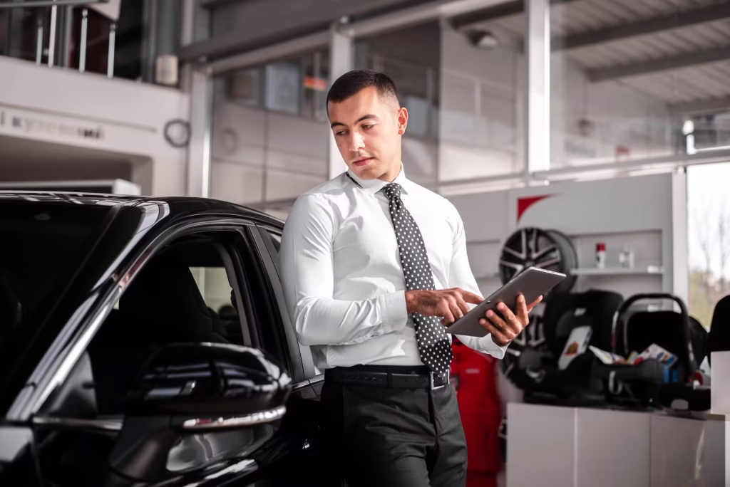 Vendedor consultando um tablet ao lado de um carro preto no showroom
