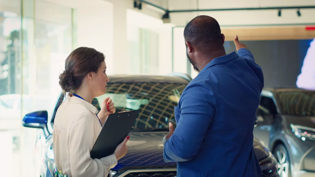 Vendedora com prancheta ouvindo um cliente que aponta para os carros