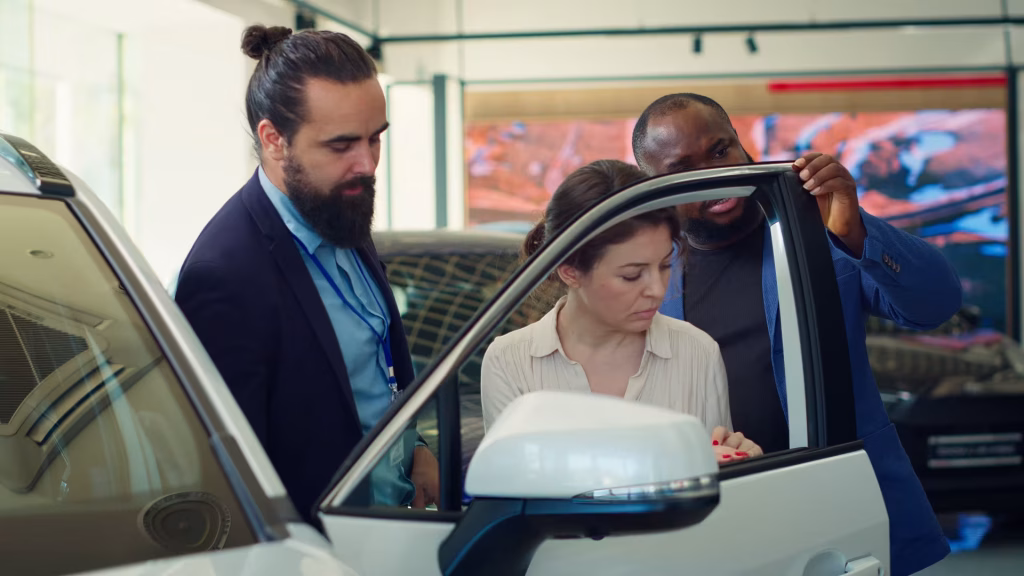 Dois vendedores mostrando a porta de um carro branco para uma cliente