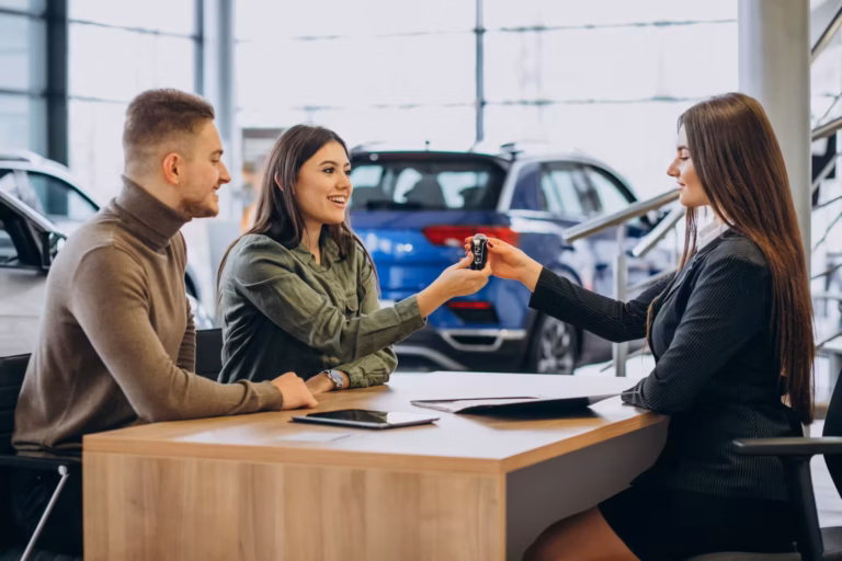 Vendedora entregando a chave do carro a um casal sentado à mesa em showroom